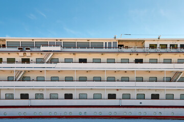 Deck of a white blue moored passenger ship on the embankment with windows to the cabins and stairs