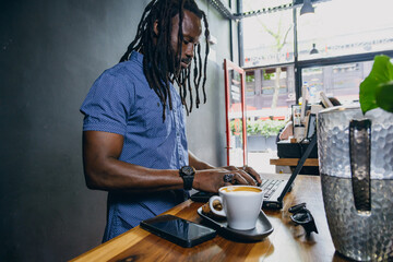 Freelance businessman with dreadlocks standing in coffee shop working on his laptop