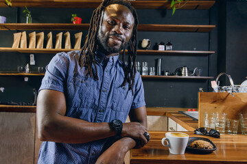 black man eating coffee with cookies, happy smiling looking at camera standing inside the restaurant