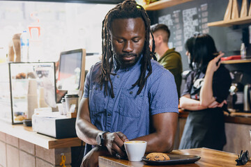 young african man with dreadlocks inside restaurant standing enjoying coffee with cookies