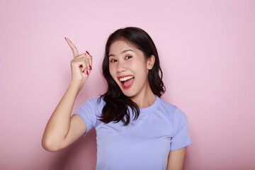 Standing and pointing happily, Portrait of a beautiful young woman in a light pink background, happy and smile, posting in stand position, Portrait of a friendly young woman smiling happily.