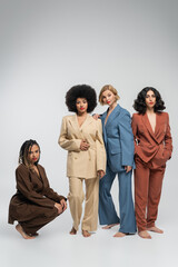 Fototapeta premium full length of multiracial barefoot girlfriends in colorful suits on grey backdrop, diverse beauty