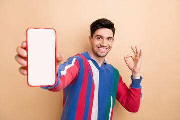 Close up shot of young man show okey symbol promoting food delivery application on smartphone display isolated over beige color background