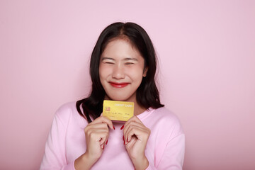 Asian woman holding a credit card in her hand Holding a debit card in hand A beautiful young woman was feeling very happy and excited. Portrait on a light pink background