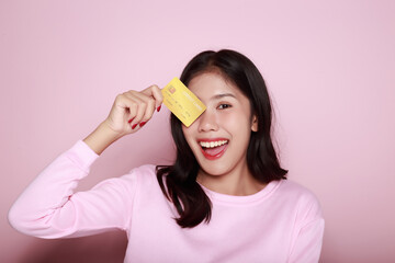 Asian woman holding a credit card in her hand Holding a debit card in hand A beautiful young woman was feeling very happy and excited. Portrait on a light pink background
