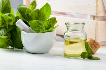 Fresh spearmint leaves and a small bottle with essential mint oil.