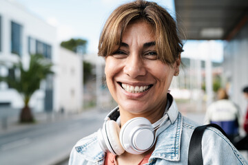 Happy Latin woman smiling in front of camera while waiting at bus station in the city - obrazy, fototapety, plakaty