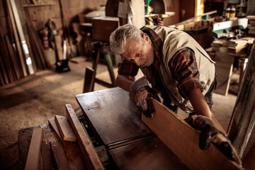 Senior male carpenter measuring wood on workbench in workshop