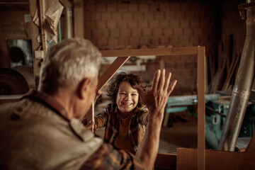 Obraz na płótnie Canvas Elderly carpenter making wood frame with little boy in workshop