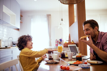 Happy little boy having breakfast with dad in kitchen at home