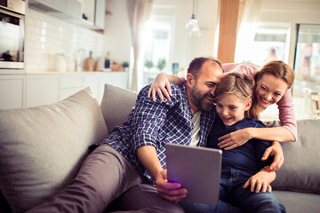 Smiling parents with little son using tablet on couch