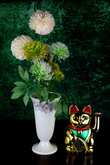 Golden Beckoning Maneki Neko Waving Cat with Artificial Flowers in a Porcelain Vase on a Wooden Surface - 679787193