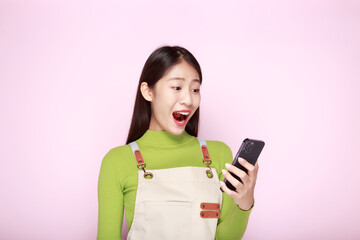 Asian woman looks surprised while holding phone in hand, Portrait of a beautiful young woman in a light pink background, happy and smile, posting in stand position.