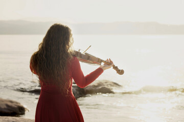 romantic scene of a woman playing the violin in front of the sea