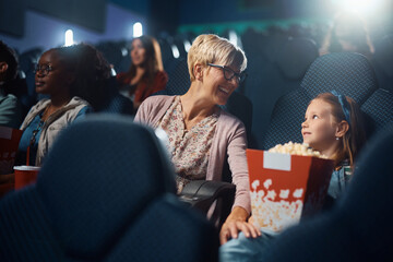 Happy grandmother and granddaughter talk before movie projection in cinema.