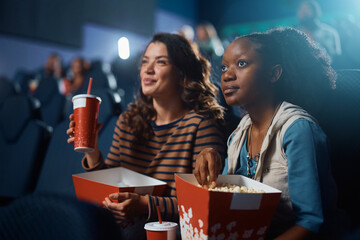 Young black woman and her female friend watching movie in cinema.