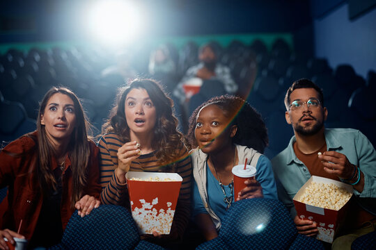 Multiracial group of friends watching suspenseful movie in theater.