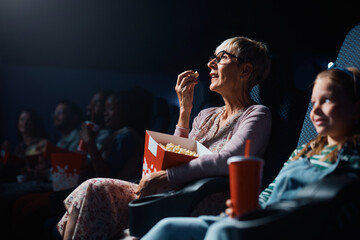 Senior woman eating popcorn during movie projection in cinema.