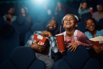 Cheerful black little girl watching movie in theater.