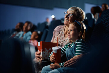 Happy little girl and her grandmother watching movie in cinema.