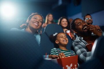 Happy black family laughing while watching funny movie in cinema.