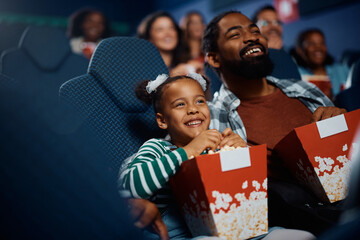 Happy black father and daughter enjoying in movie projection in theater.