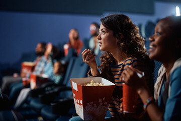 Young woman eats popcorn while watching suspenseful movie in cinema.