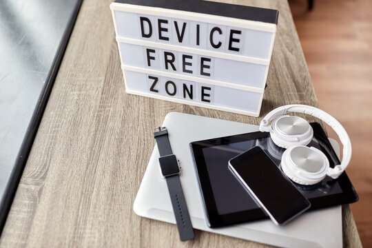 digital detox and technology concept - close up of device free zone words on light box and different gadgets on table at home