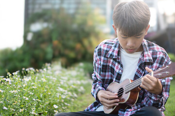 Asian cute boy plays ukulele in front yard of his house in the morning with the sunshine, soft and...