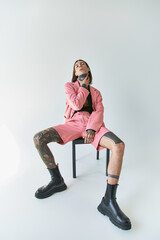 Fototapeta premium stylish sexy man in pink blazer and shorts sitting on chair and looking at camera with hand on neck