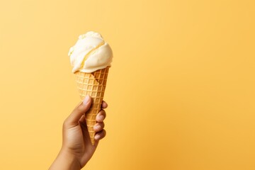 Close up of a hand holding a tasty vanilla milk ice cream cone on a solid pastel color background