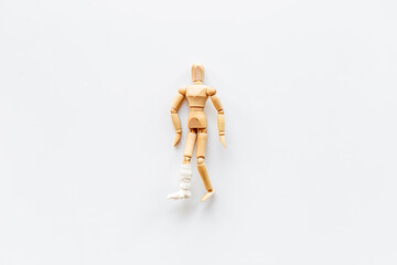 Wooden dummy man with leg broken - leg in bandage. Medical insurance and healthcare concept