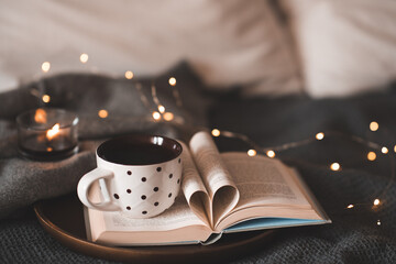 Cup of coffee with polka dots stay on open paper book folded pages in heart shape on tray over Christmas lights close up. Winter holiday season. - obrazy, fototapety, plakaty