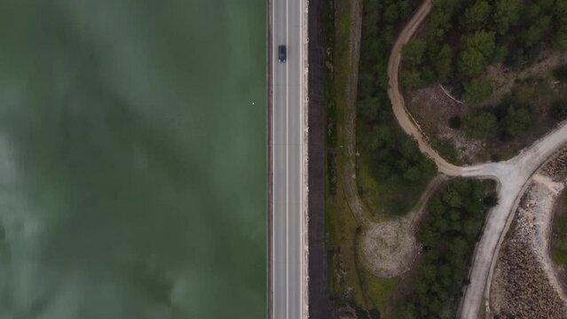 Video from above traveling along a road over a dam wall as a car drives along it