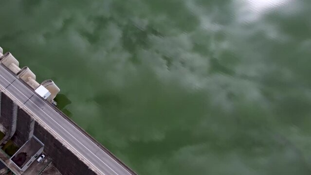 Drone video of a road over a dam wall with the reservoir filled with water reflecting the clouds