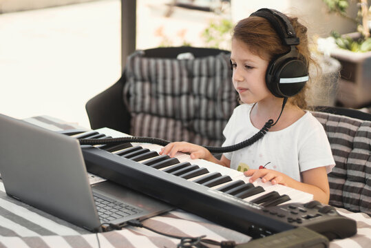 A young white Caucasian girl wearing headphones and playing a MIDI keyboard connected to a laptop personal computer