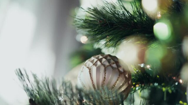 A golden ball ornament on a decorated Christmas tree with branches and lights.