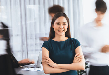 Young Asian businesswoman portrait poses confidently with diverse coworkers in busy meeting room in motion blurred background. Multicultural team works together for business success. Concord