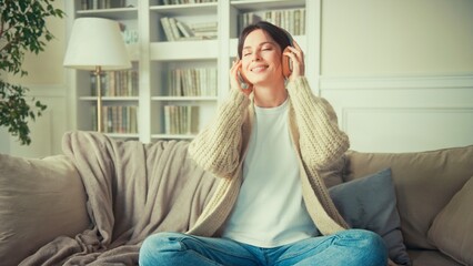Fototapeta premium Portrait of young woman relaxing at home and listening music. Girl sitting on sofa. Relaxation, Meditation and Mindfulness