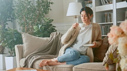 Obraz premium Portrait of Pretty Young Business Woman Drinking Coffee And Working Notebook From Home in Cozy Sunny Living Room. Young woman using laptop computer on sofa. Browsing on social media relaxed