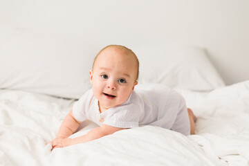 Adorable baby boy in white sunny bedroom. Newborn child relaxing in bed. Nursery for young children. Textile and bedding for kids. Family morning at home.