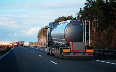 Petrol cargo truck driving on highway hauling oil products. Fuel delivery transportation and logistics concept. Compressed gas carrier truck rear view on a highway. Dangerous goods shipping in bulk