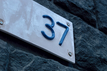 Number 37 building retro style white ceramic number plate with blue numbers, on the stone bricks background.