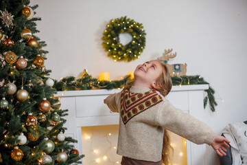 An adorable little girl of 5 years old with long curly hair and blue eyes decorates a Christmas tree. Holidays. New Year. The winter vacation.