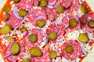 uncooked pizza with sausage, blue onions and cucumbers, close-up