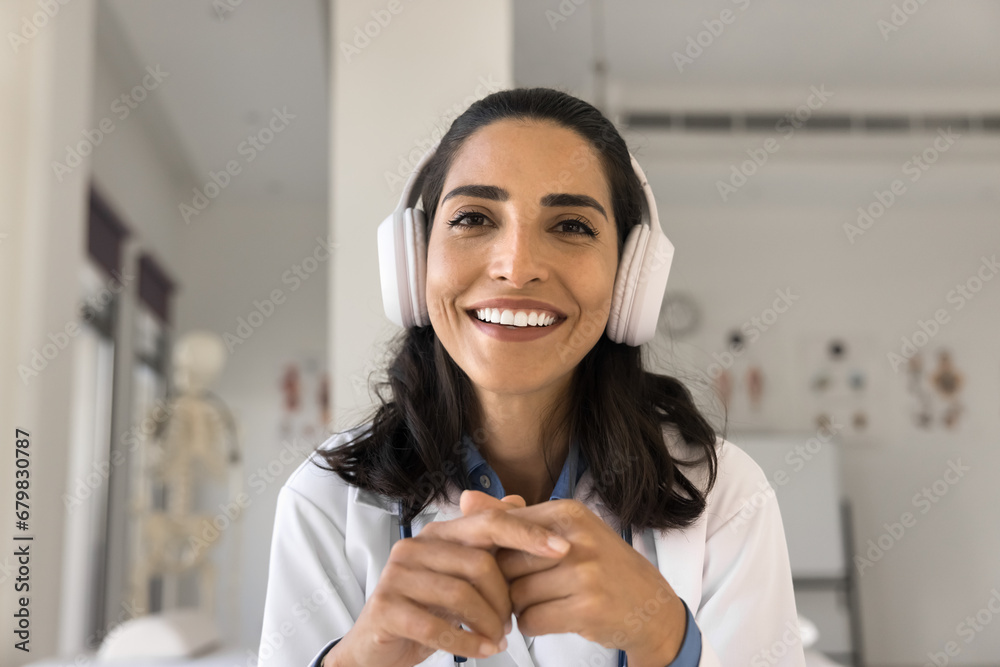 Wall mural Happy beautiful Latin doctor woman in headphones head shot portrait. Young practitioner, medical therapist giving online consultation on video call, speaking from screen with toothy smile