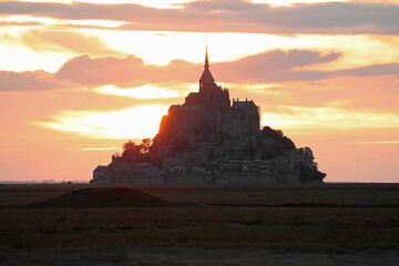 sunset with fiery sky with red clouds and the silhouette of the ancient abbey of Mount Saint Michel...