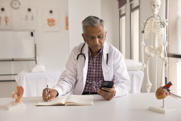 Serious elder Indian doctor man giving medical consultation on Internet, chatting with patient on smartphone, using Internet technology, healthcare application on mobile phone