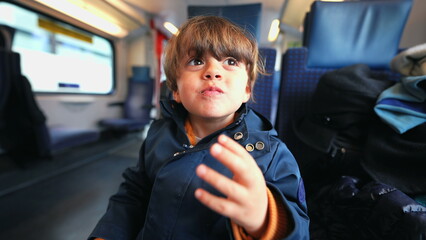 Caucasian boy seated in train relishing a butter biscuit, indulging in a cookie treat during his...