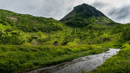 Fototapeta na wymiar The scenic river goes through the Vachkazhets valley at Kamchatka krai, Russia, with beautiful mountains and grass fields around.